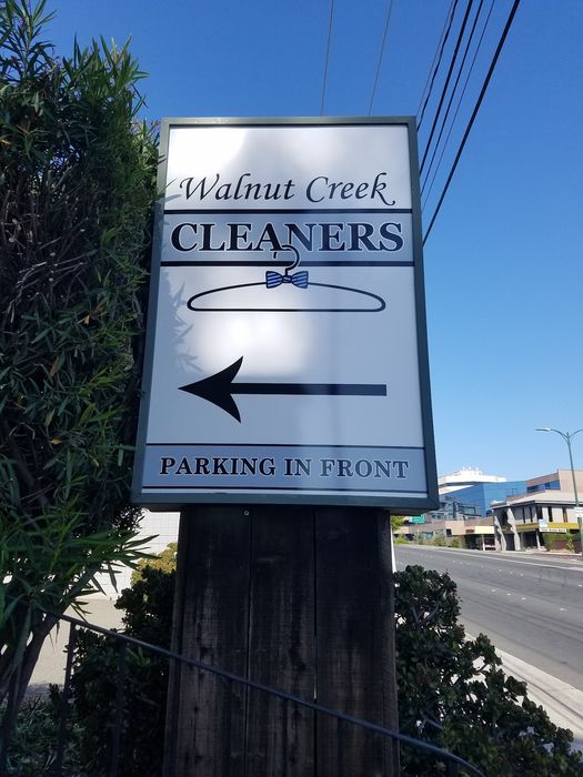 Street sign reading Walnut Creek Cleaners with a hanger and bow tie logo, an arrow, and Parking in Front
